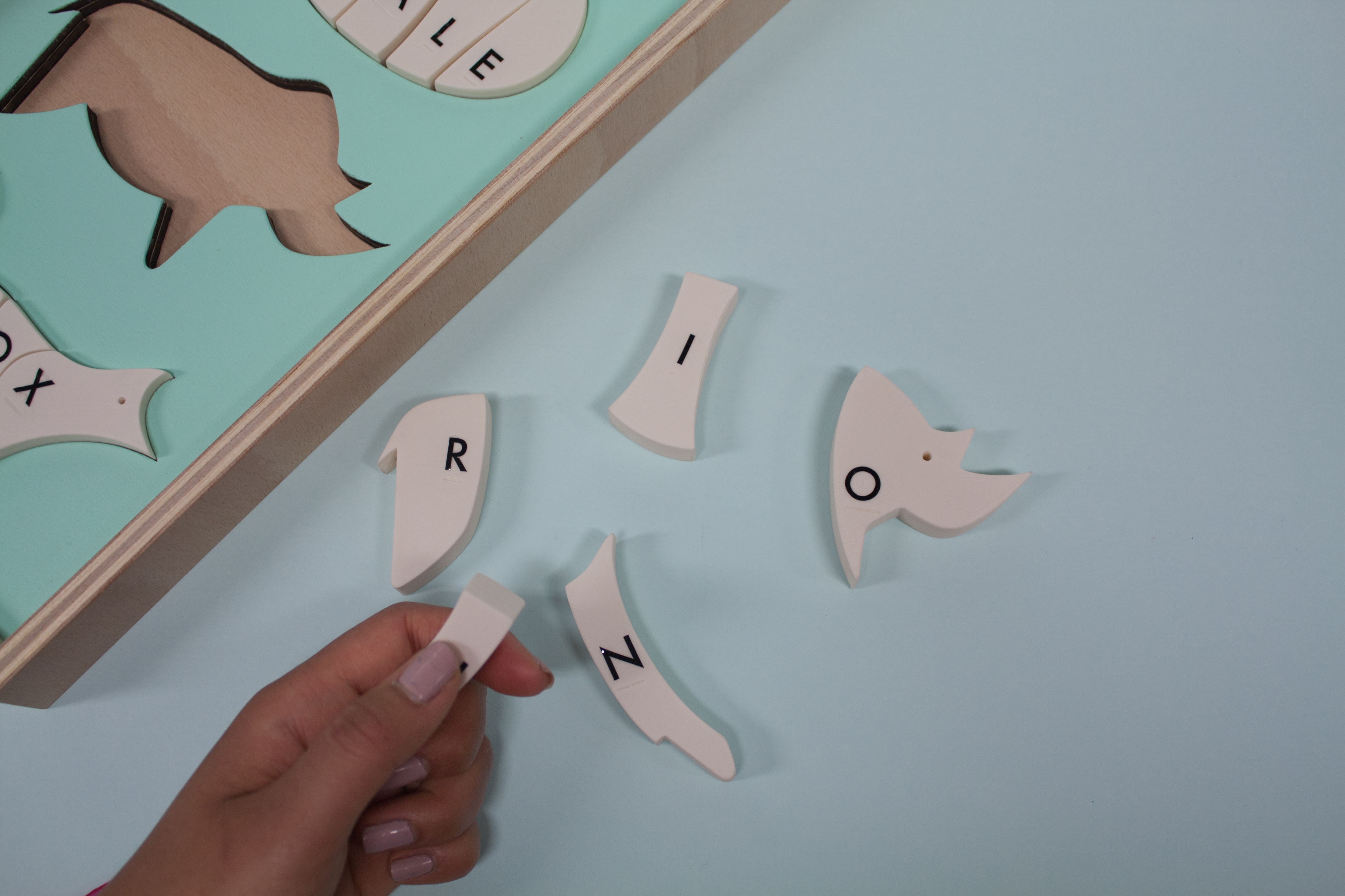 Eine Hand sucht durch erfühlen der Buchstaben in Braille-Schrift das passende H Stück zum Rhinozeros.